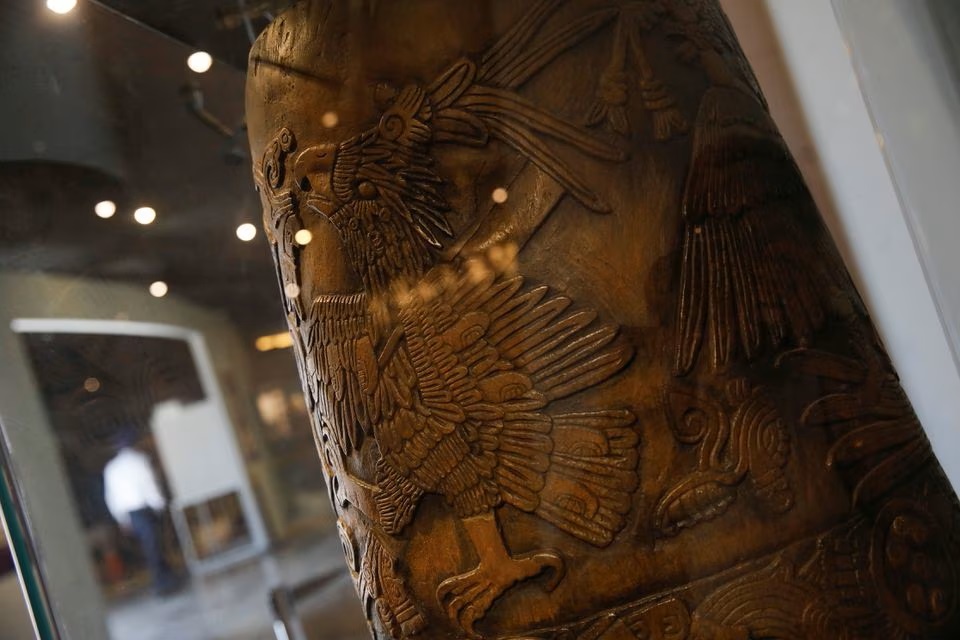 Patung kopal berukir yang menggambarkan tlaloque, atau penolong dewa hujan Aztec Tlaloc, digambarkan (kiri) bersama dengan topeng kayu, tongkat kerajaan, dan kendi air, di samping pot keramik model Tlaloc (kanan) dengan benda serupa perhiasan, bagian dari pameran "Lambang Para Dewa, kayu di Templo.